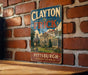 A vintage-style metal sign with the text "CLAYTON THE FRICK PITT'SBURGH PENNSYLVANIA" displayed on a brick wall.