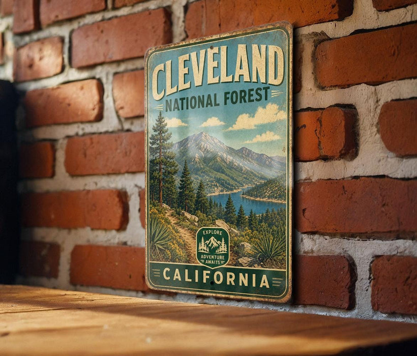 A vintage metal sign for the Cleveland National Forest in California, featuring a scenic mountain landscape with pine trees and a lake.