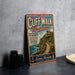 A vintage-style metal sign for Cliff Walk, Rhode Island, featuring a scenic coastal landscape with a castle and a winding path.