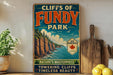 A vintage-style sign for Cliffs of Fundy Park, featuring a scenic image of the park's cliffs and surrounding nature.
