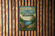 A vintage metal sign for the Cockaponset State Forest in Connecticut, featuring a scenic landscape with pine trees, a lake, and mountains.