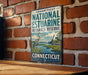 A vintage metal sign for the Connecticut National Estuarine Research Reserve, featuring a blue heron and a lighthouse, is mounted on a brick wall.