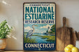 A vintage-style sign for the Connecticut National Estuarine Research Reserve, featuring an illustration of a heron in a grassy area with a lighthouse in the background.