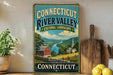 A vintage-style sign for the Connecticut River Valley, featuring a scenic landscape with a river, buildings, and mountains.