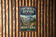 A vintage metal sign with the text "Continental Divide Trail Montana" hanging on a wooden wall.