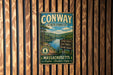 A vintage metal sign for Conway State Forest, featuring a scenic image of pine trees and a river, mounted on a wooden wall.