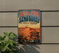 A vintage-style metal sign for the Coral Pink Sand Dunes State Park in Utah, featuring a desert landscape with mountains and a cactus in the foreground.