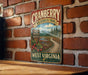 A vintage-style metal sign for the Cranberry Wilderness Trail in West Virginia, featuring a scenic landscape with a winding path, trees, and red berries.