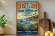 A vintage-style metal sign for Crystal Cove State Marine Conservation Area in California, featuring a coastal landscape with a fish, palm trees, and a wooden paddle.