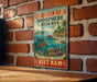 a vintage-style sign with a tropical beach scene, including a turtle, palm trees, and a boat, mounted on a brick wall.