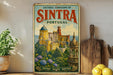 a vintage-style metal sign with a colorful illustration of a castle, surrounded by nature, placed on a shelf next to a wooden cutting board and some potted plants.