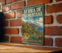 A vintage metal sign with a scenic illustration of the Serra de Tramuntana, a famous coastal town in Spain, is displayed on a brick wall.
