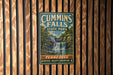 A vintage metal sign for Cummins Falls State Park in Tennessee, featuring a waterfall and lush greenery.