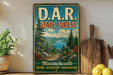 A vintage-style metal sign for the State Forest in Massachusetts, featuring a scenic landscape with pine trees, a lake, and mountains.