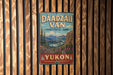 A vintage-style metal sign for Dáadzálí Van, located in Yukon, Canada, hangs on a wooden wall.