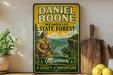 A vintage-style metal sign for the Missouri State Forest, featuring a man in a hunting outfit and a scenic landscape.