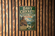 a vintage metal sign with the text "DAVY CROCKETT NATIONAL FOREST TEXAS" and an illustration of a man with a rifle in a forest setting.