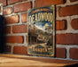 A vintage-style metal sign for Deadwood, a historic district in Dakota, South Dakota, featuring an illustration of a saloon and a horse-drawn carriage.