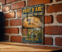 a vintage-style metal sign with a cave painting and text, mounted on a brick wall.