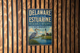 A metal sign with the text "DELAWARE NATIONAL ESTUARINE RESEARCH RESERVE DELAWARE" and an illustration of a bird standing on a grassy area near a lighthouse.