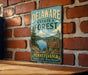 A vintage metal sign for the Delaware State Forest in Pennsylvania, featuring a scenic landscape with pine trees, a lake, and mountains.