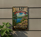 A vintage-style metal sign for Devil's Lake State Park in Wisconsin, featuring a scenic landscape with a lake, mountains, and trees.