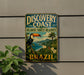 A vintage-style metal sign with a tropical landscape and a toucan, advertising the Discovery Coast Atlantic Forest Reserve in Brazil.