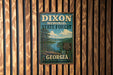 A vintage metal sign for Dixon Memorial State Forest in Georgia, featuring a scenic landscape with pine trees, a lake, and mountains.