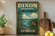 A vintage-style metal sign for the Dixon Memorial State Forest in Georgia, featuring a scenic landscape with pine trees, a lake, and mountains.