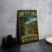 A vintage-style sign for the "Driftless Area" in Wisconsin, featuring a scenic landscape with a river and a barn.