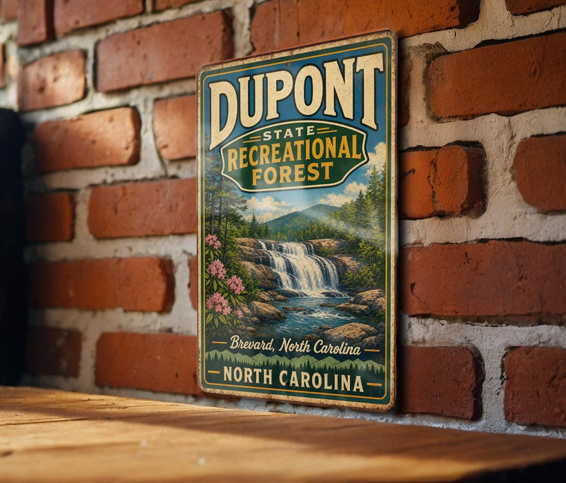 A vintage-style metal sign for DuPont State Recreational Forest in North Carolina, featuring a scenic image of a waterfall surrounded by pine trees and mountains.