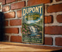 A vintage-style metal sign for DuPont State Recreational Forest in North Carolina, featuring a scenic image of a waterfall surrounded by pine trees and mountains.