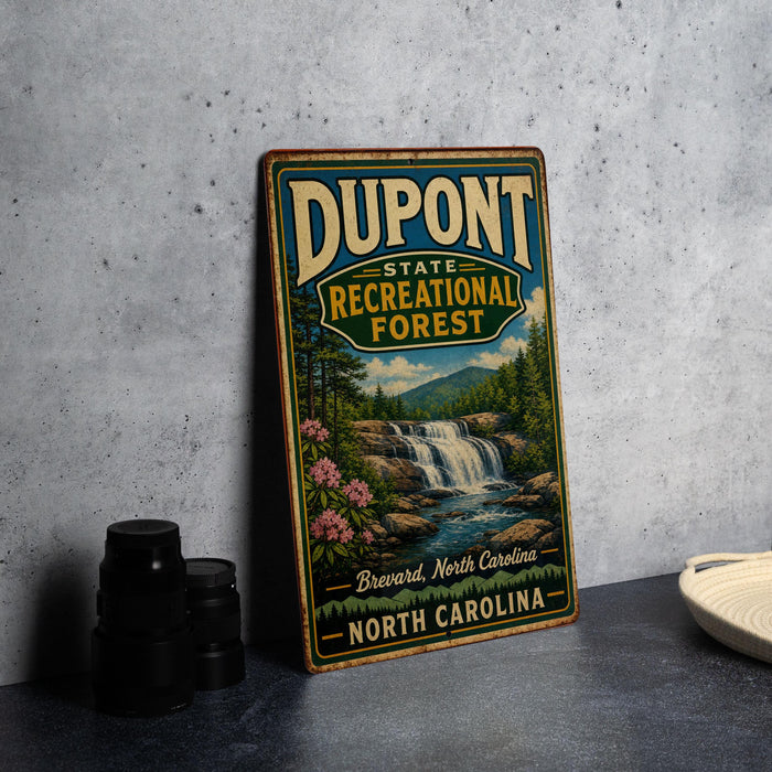 A vintage-style sign for DuPont State Recreational Forest in North Carolina, featuring a scenic image of a waterfall and surrounding landscape.