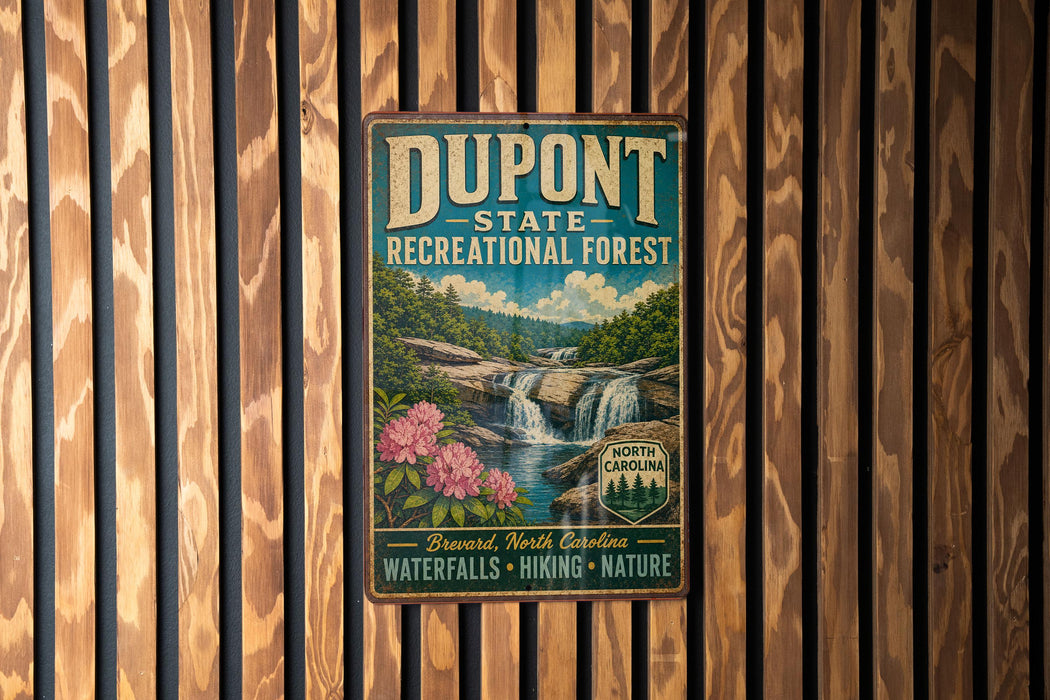A vintage-style metal sign for DuPont State Recreational Forest, featuring a waterfall and flowers, is displayed on a wooden wall.