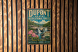 A vintage-style metal sign for DuPont State Recreational Forest, featuring a waterfall and flowers, is displayed on a wooden wall.