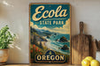 A vintage-style metal sign for Ecola State Park in Oregon, featuring a scenic coastal landscape with mountains, trees, and the ocean.