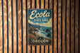 A vintage-style metal sign for Ecola State Park in Oregon, featuring a scenic landscape with mountains, trees, and a body of water.