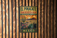 a metal sign with a desert landscape and cacti, mounted on a wooden wall.