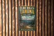 A vintage metal sign for Elbe Hills, Tahoma State Forest in Washington, featuring a scenic mountain landscape.