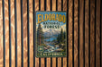 A vintage metal sign for the Eldorado National Forest in California, featuring a scenic landscape with a mountain, pine trees, and a river.