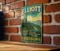 A vintage metal sign for Elliott State Forest, featuring a scenic landscape with pine trees and mountains, mounted on a brick wall.