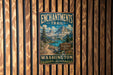 A vintage metal sign for the Enchantments Trail in Washington, featuring a scenic mountain landscape with a lake and pine trees.