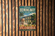 A vintage-style sign for Ernest Hemingway's home in Key West, Florida, featuring a palm tree and a house.