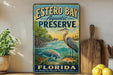 A vintage-style metal sign for Estero Bay Aquatic Preserve in Florida, featuring illustrations of various marine life such as a heron, a manatee, and a dolphin.