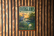 A vintage-style metal sign for Everglades National Park, featuring a bird, water lilies, and a sunset landscape, is mounted on a wooden wall.