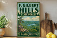 a vintage-style sign for F. Gilbert Hills State Forest in Massachusetts, with a scenic landscape of mountains, trees, and a river.
