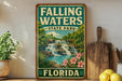 A vintage-style sign for Falling Waters State Park in Florida, featuring a waterfall and tropical foliage, is displayed on a shelf next to a wooden cutting board and some potted plants.