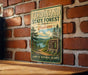 A vintage-style metal sign for the Ferndand State Forest in Indiana, featuring a scenic landscape with pine trees, a lake, and mountains.