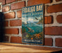 a vintage-style metal sign for Fidalgo Bay Aquatic Reserve, which is located in Washington. The sign is hanging on a brick wall and depicts a seascape with a sailboat, fish, and marine life.