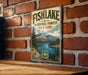 A vintage-style metal sign for Fish Lake National Forest in Utah, featuring a scenic landscape with mountains, a lake, and pine trees.